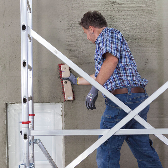 Nach dem Verputzen der Wand raut der Heimwerker den frischen Kalkzementputz horizontal mit einem Straßenbesen auf.