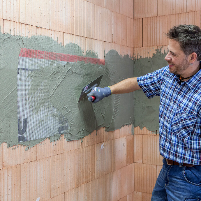 Der Heimwerker bettet mit einer Zahnkelle das Armierungsgewebe in den frischen Putz auf den XPS-Platten ein.