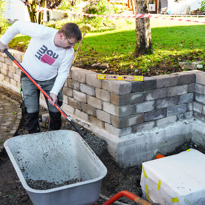 Die Baugrube mit der Sickerbox und eingebautem Drainagerohr wird mit Kies aufgefüllt.