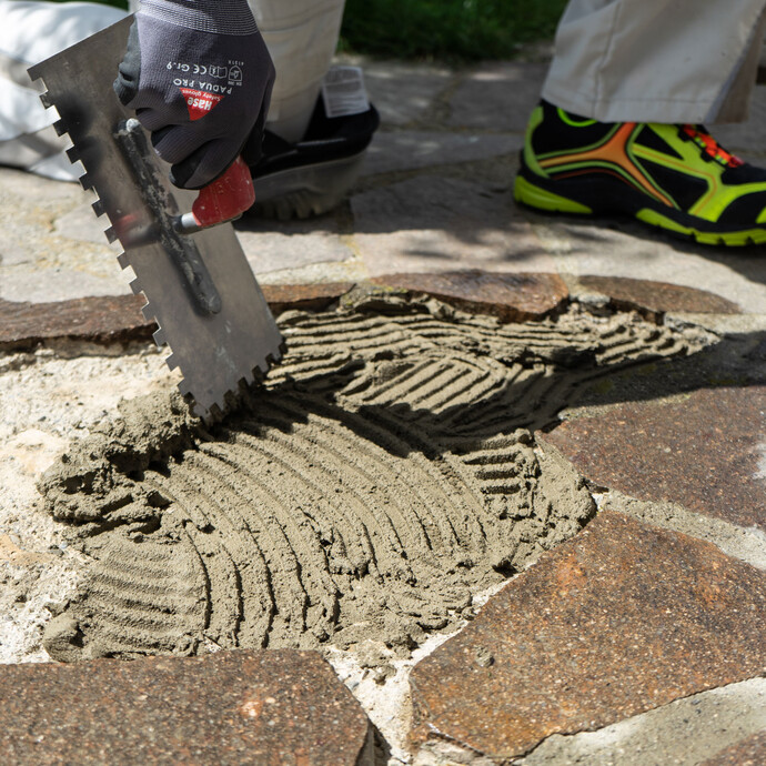 Frisch angerührter Steinkleber Trass wird mit einer Zahnkelle vollflächig auf den angefeuchteten Untergrund aufgetragen.