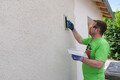 Le bricoleur structure l'enduit fouetté de Munich avec une planche à râper en plastique en effectuant des mouvements circulaires.