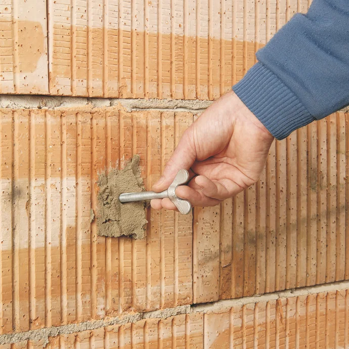 Manns Hand montiert eine Dübelanker in eine gemauerte Wand, bereit für DIY-Projekte, Baumit-Selbermachen.