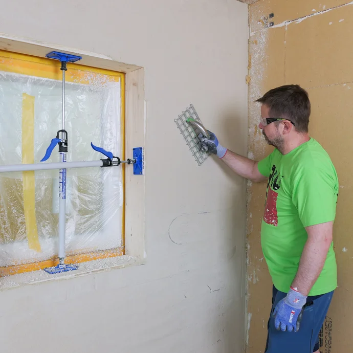 Mann reibt die verputzte Wand mit einem Giterrabott ab.
