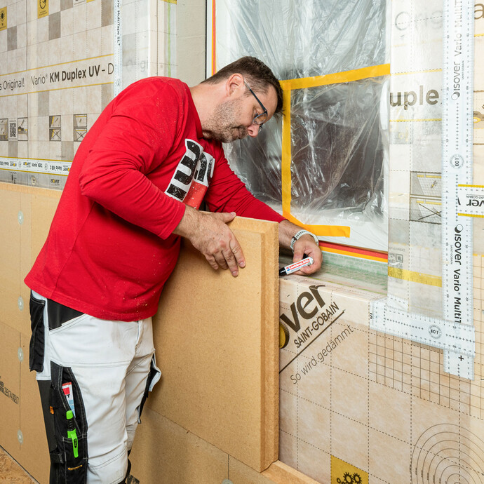 Heimwerker zeichnet mit einem Stift den Ausschnitt einer Holzfaserdämmplatte an einem Fenster an – Öffnungsausschnitt für Innendämmung vorbereiten.