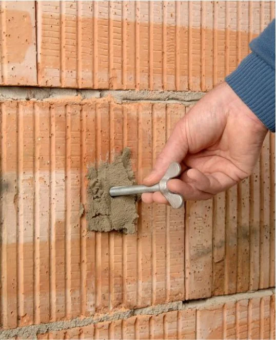 Hand verteilt Mörtel auf Ziegelwand für eine stabile Befestigung.