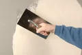 Person glättet Wand mit Glättkelle und Putz, zeigt Anwendungstechnik für Heimwerkerprojekte mit Baumit-Produkten.