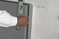 Une main aligne un panneau isolant sur un mur à l'aide d'un niveau à bulle.