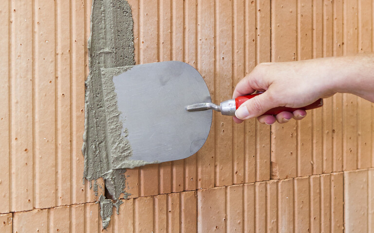 Detailfoto: Die Spalte im Mauerwerk wird mit einer Stuckateurspachtel und dem Mörtel verschlossen.