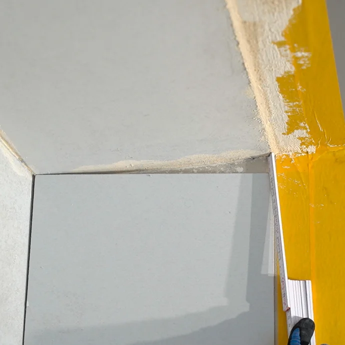 Mit einem Meterstab wird das Maß ermittelt, sodass der Anschlusskeil an der Wand bündig zur Decke zugeschnitten werden kann.