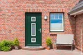 Façade en briques rouges avec une porte d'entrée et des fenêtres vertes, agrémentée de plantes et d'un banc, idéale pour un projet de rénovation en bricolage.