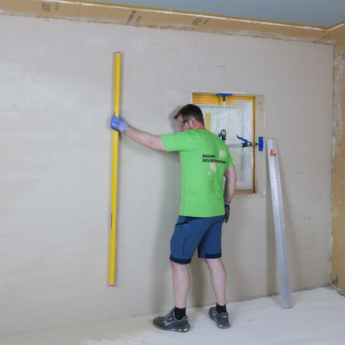 Die frisch verputzte Wand wird mit einer langen Wasserwaage geprüft, falls es noch unebene Stellen an der Wand gibt.