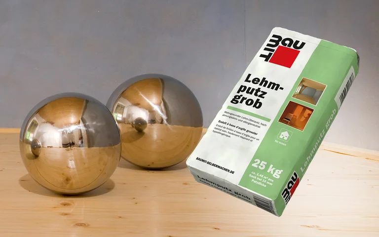 Papiersack Baumit Lehmputz Grob auf Holz, reflektierende Metallkugeln, geeignet für DIY-Putzarbeiten im Innenbereich.