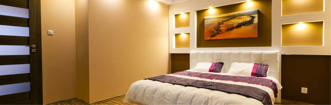 Chambre &agrave; coucher au design moderne, avec un &eacute;clairage chaleureux et un rev&ecirc;tement mural contrast&eacute; derri&egrave;re le lit.