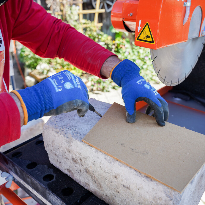 Handwerker zeichnet auf den Stein mit Stift und Karton die benötigte Schnittlinie an. Der Naturstein liegt auf dem Tisch der Tischsäge von Norton Clipper.