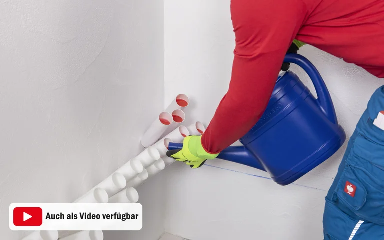 Person mit Schutzhandschuhen befüllt mit einer blauen Gießkanne Injektionstrichter in einer Wand zur Horizontalabdichtung.