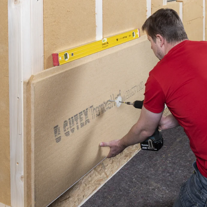 Mann montiert Holzfaser-Dämmplatte an Wand, verwendet Wasserwaage zur Ausrichtung. Perfekt für DIY-Isolierungsprojekte.