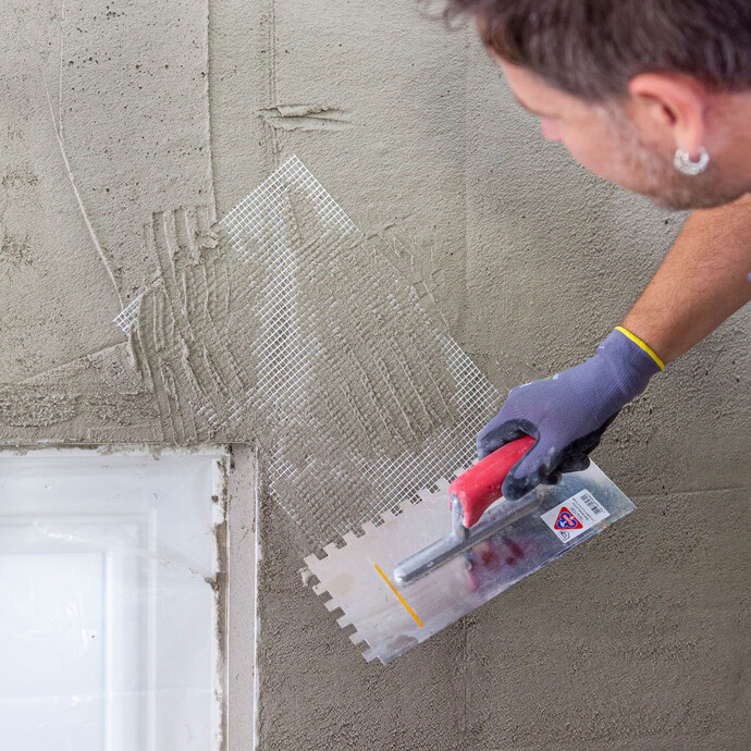 Beim Verputzen einer Wand wird im Eckbereich ein Streifen Armierungsgewebe in den frischen Putz eingesetzt und eingespachtelt.