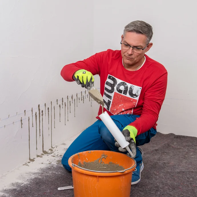 Handwerker füllt Baumit Beton- und Reparaturspachtel in den Injektionstrichter.