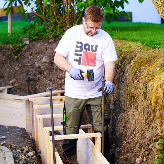 Mit Erdnägeln wird die Schalung für das Fundament der Gartenmauer gesichert, damit die Schalungselemente nicht verrutschen können.
