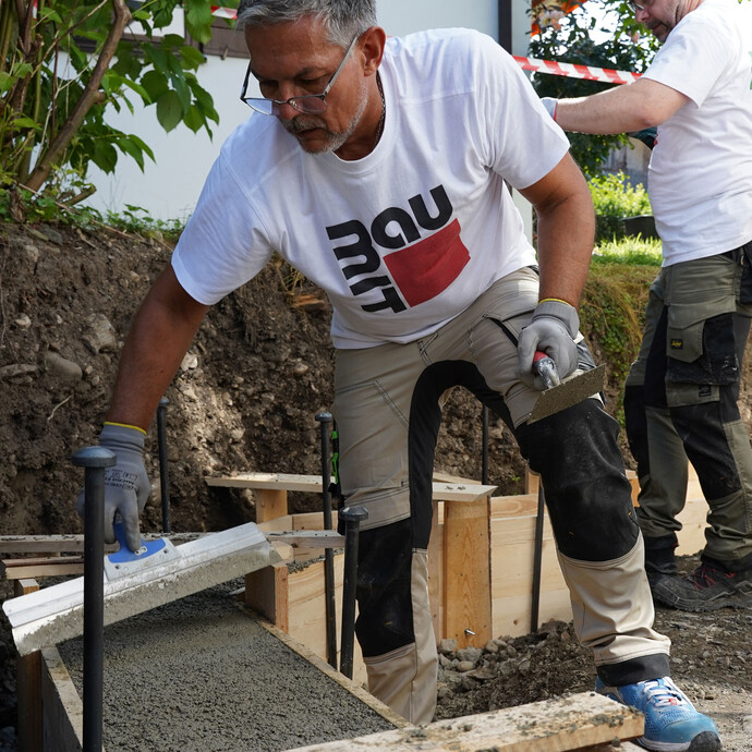 Die Oberfläche des frischen Betons in der Schalung wird eben mit einem Flächenspachtel abgezogen. Ein Fundament betonieren ist anstrengend, daher sind mehrere Personen von Vorteil.