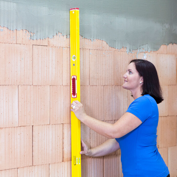 Frau prüft die Wand, ob sie uneben ist, mit einer langen Wasserwaage.