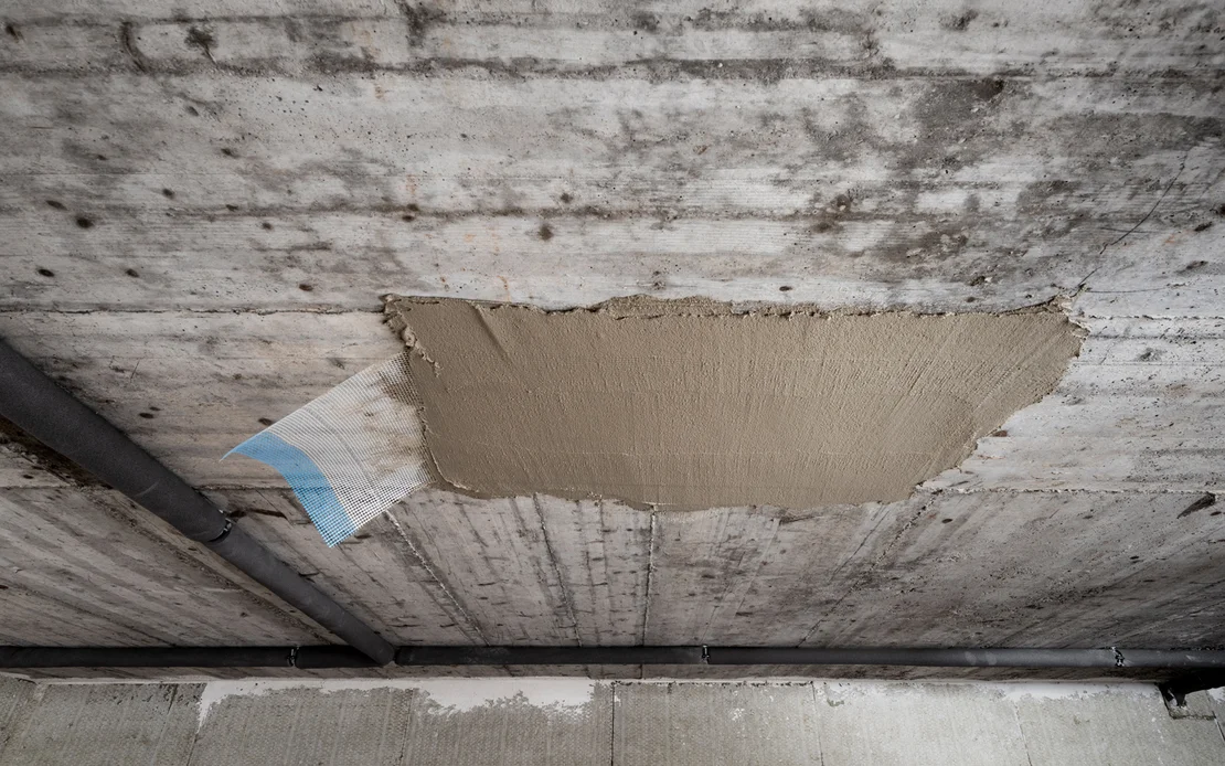 Decke mit frischem Betonreparaturm&ouml;rtel ausgebessert, sichtbar heller Fleck in dunkler Betonfl&auml;che, Heimwerkerprojekt.