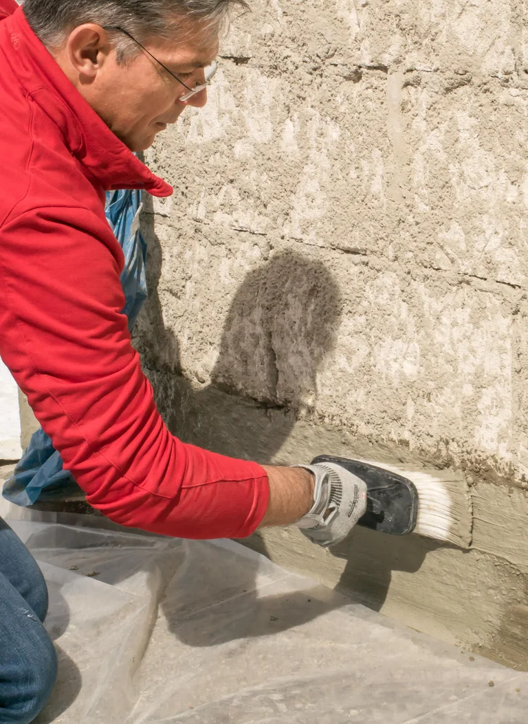 Un homme applique de l'enduit sur un mur et donne des conseils de bricolage pour la rénovation de façades avec les produits Baumit.
