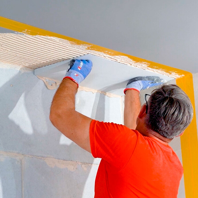 Heimwerker setzt den Anschlusskeil an der Decke in den frisch aufgetragenen Putz.