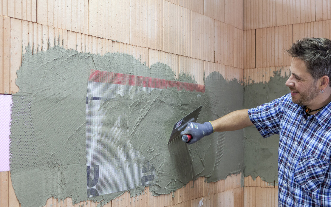 Der Heimwerker bettet mit einer Zahnkelle das Armierungsgewebe in den frischen Putz auf den XPS-Platten ein.