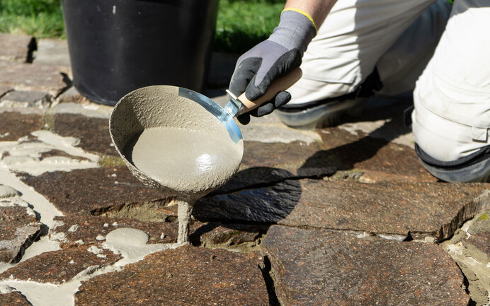 Pflasterfugenmörtel mit Gipserkelle o.ä. in den Fugen der Natursteine einbringen.