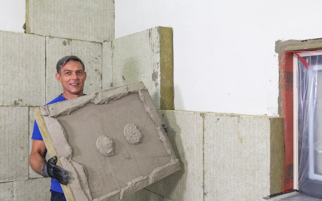 Un bricoleur pose un panneau isolant sur un mur &agrave; l&rsquo;aide de mortier-colle pour une isolation thermique efficace.