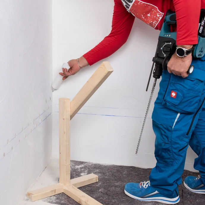 Handwerker steckt Injektionstrichter in das Bohrloch der Innenecke der Wand.