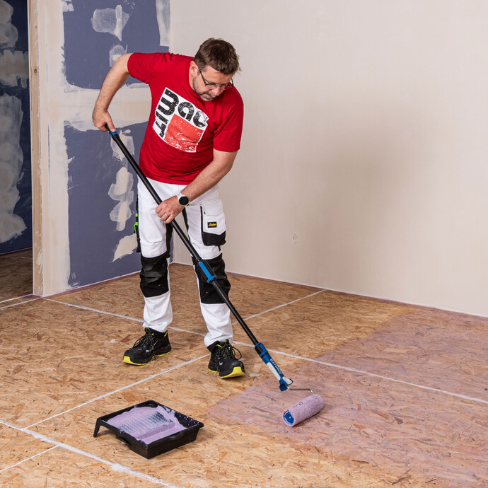 L'artisan Baumit apprête le sol en panneaux d'aggloméré avec une couche de fond adaptée - dans ce cas, avec Supergrund.