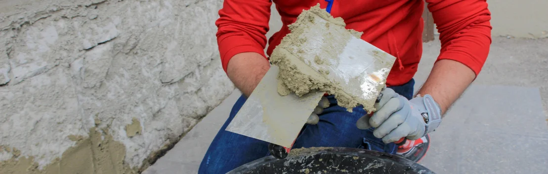 Un bricoleur applique de l'enduit au mur &agrave; l'aide d'une truelle ; un projet de r&eacute;novation facile gr&acirc;ce aux produits Baumit.
