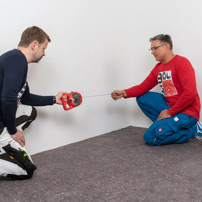 Zwei Handwerker markieren mit einer Schlagschnur die erste Bohrlochreihe.