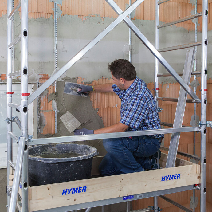 Heimwerker steht auf dem Gerüst und verputzt die Wand mit Kalkzementputz.