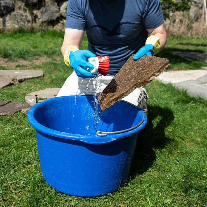 Natursteinplatte wird mit einer Bürste und Wasser über einer blauen Wanne gründlich gereinigt.