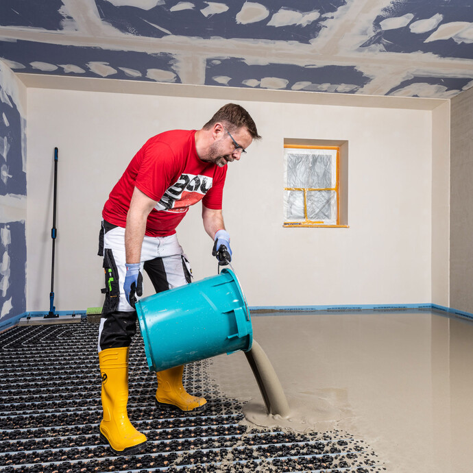 L'homme vide la masse de nivellement ou d'égalisation mélangée sur le chauffage au sol installé.