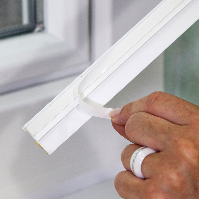 Photo de détail : la bande adhésive est retirée de l'arrière de la baguette de finition.