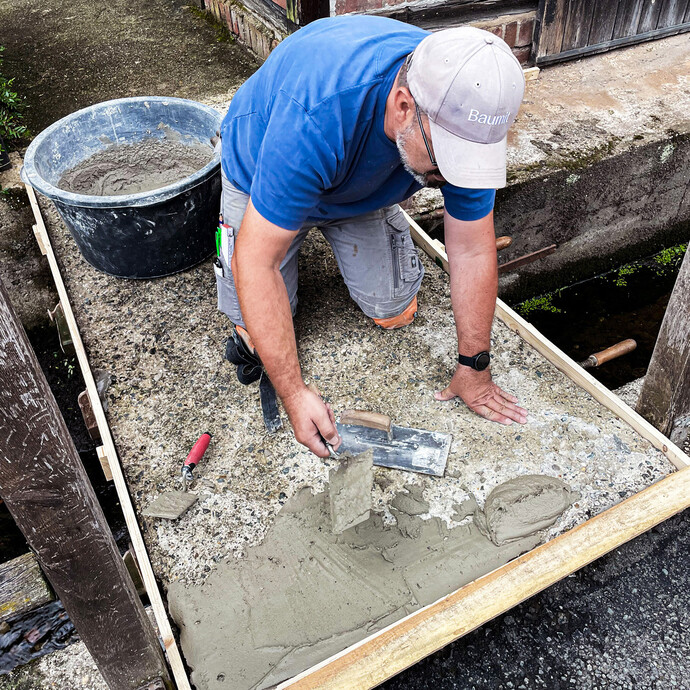 Handwerker trägt Gefällespachtel mit Glättkelle auf Betonfläche in Holzschalung auf.