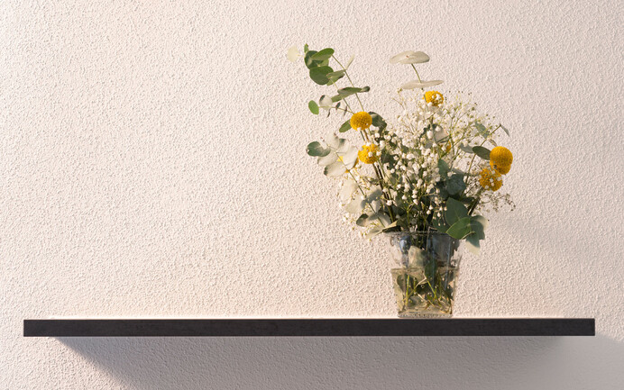 Décorer les murs avec l'enduit noble InStyle Edelweiss, sain pour l'habitat, à la structure finement feutrée, décoré d'une étagère et d'un bouquet de fleurs.