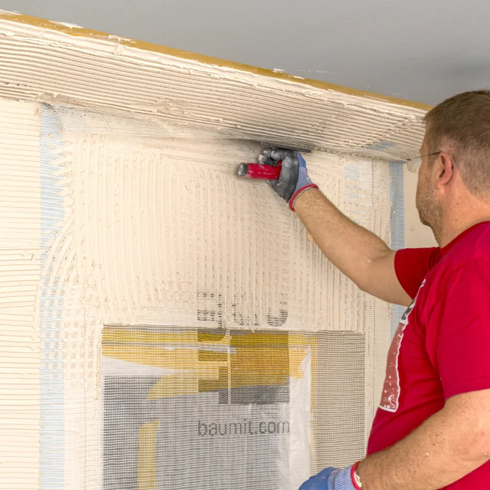 Heimwerker verspachtelt Wand mit Putz, Schritt in der Wandvorbereitung, Baumit-Tipps für ein perfektes Renovierungsergebnis.