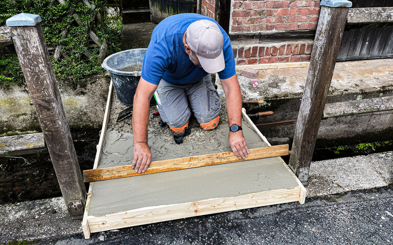 Handwerker zieht Gefällespachtel mit Abziehlatte in Holzschalung ab.