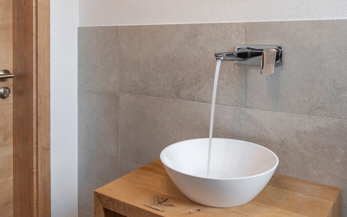 Lavabo blanc moderne avec eau courante sur sideboard en bois mis en scène avec des panneaux muraux gris nobles avec un enduit noble sain pour l'habitat en structure feutrée. 