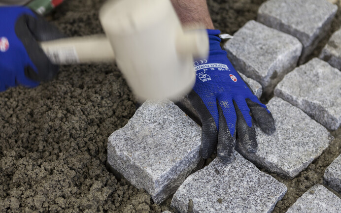 Granitpflasterstein mit Gummihammer in den frischen Pflasterdrainmörtel einklopfen