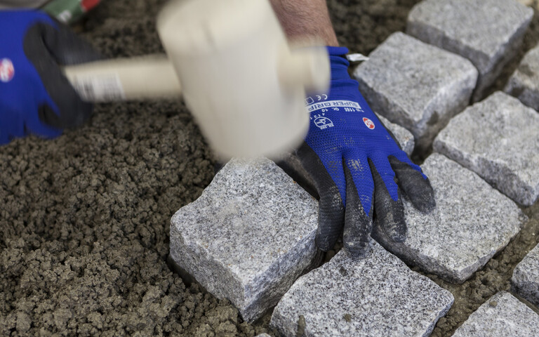 Granitpflasterstein mit Gummihammer in den frischen Pflasterdrainmörtel einklopfen