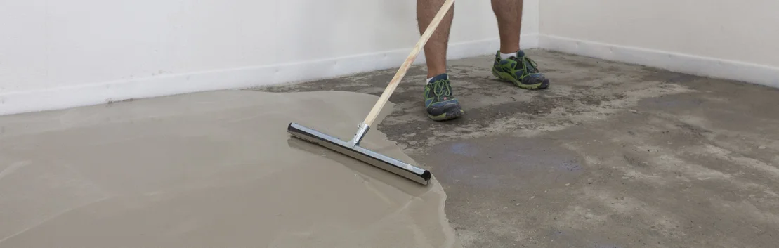Le bricoleur &eacute;tale un enduit autonivelant &agrave; l'aide d'une raclette sur un sol en b&eacute;ton afin d'obtenir une surface lisse.