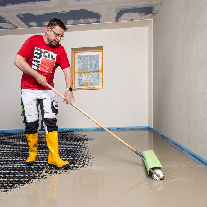 Le bricoleur purge la masse d'égalisation installée à l'aide d'un rouleau à pointes (également appelé rouleau hérisson).