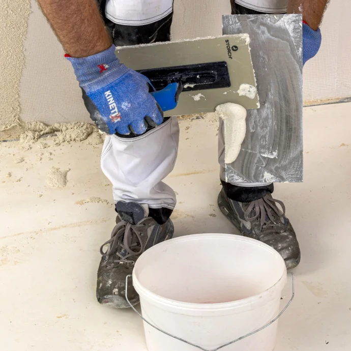 Heimwerker spachtelt mit Kelle Wand; Putz aus Eimer auftragen und glätten, Schritt-für-Schritt für DIY-Projekte.