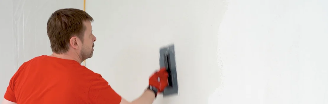 Un bricoleur applique de l’enduit sur le mur à l’aide d’une taloche de lissage afin d’obtenir une surface lisse.